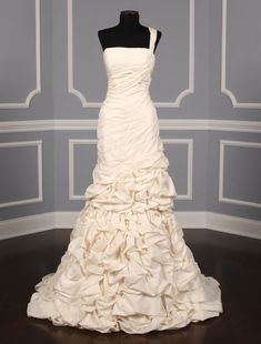 a white wedding dress on display in front of a gray wall and wooden flooring