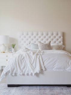 a white bed sitting in a bedroom next to a lamp on a dresser and mirror