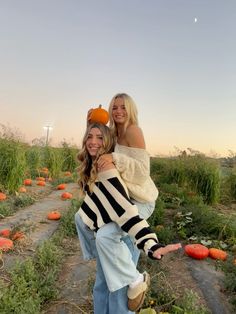 two women standing in a field full of pumpkins with one holding the other's head