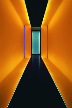 an empty hallway with yellow walls and black flooring is lit by blue light at the end