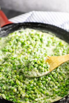 a pan filled with peas and sauce on top of a wooden spoon in the skillet