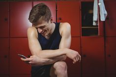 a young man sitting on the floor looking at his cell phone while holding his arm over his shoulder