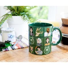 a green coffee mug sitting on top of a wooden table next to a potted plant