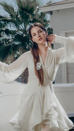 a woman standing in front of a car wearing a white dress and holding her hair up