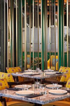 an empty restaurant with yellow chairs and green wall dividers behind the tables, along with place settings for four people