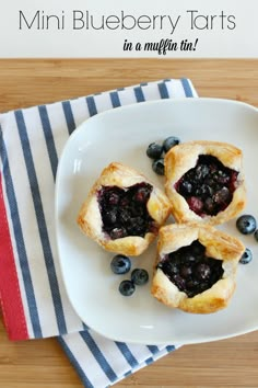 mini blueberry tarts in a muffin tin on a white plate with striped napkin