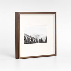 a black and white photo in a wooden frame with trees on the mountain behind it