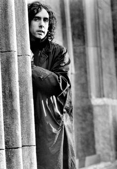 a black and white photo of a man leaning against a column