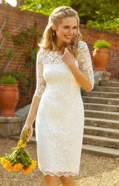 a woman in a white lace dress is walking down some steps and holding a yellow bouquet