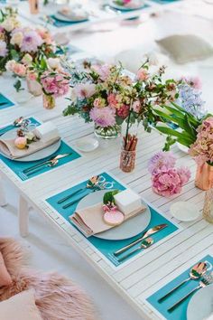 the table is set with pink and blue flowers in vases, silverware, napkins, and utensils