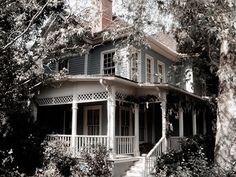 an old house is surrounded by trees and shrubbery in the foreground, with stairs leading up to the second story