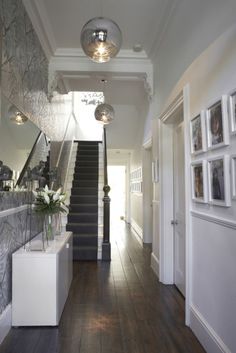 an image of a hallway with stairs and pictures hanging on the wall, in front of a mirror