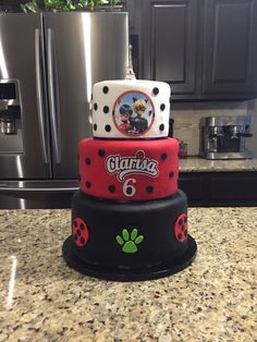 three tiered cake with ladybug and paw print on the top, sitting on a kitchen counter