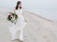 a woman in a white dress holding a bouquet on the beach