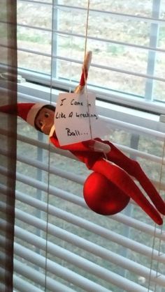 an elf hanging from the side of a window with a note attached to his head