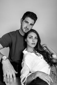 a man sitting next to a woman on top of a chair in front of a wall