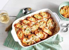 a casserole dish with cheese and vegetables in it next to two glasses of wine