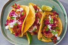 three tacos on a blue plate with limes and cilantro garnish