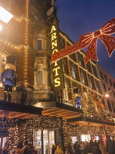 people are walking in front of a building decorated with lights and christmas decorations at night