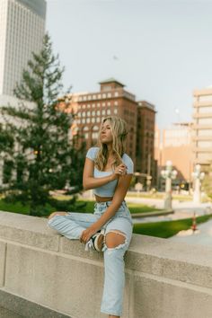 a woman is sitting on a ledge with her legs crossed and looking off to the side