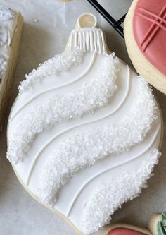 decorated cookies with icing and decorations on top of a white tablecloth, next to an ornament that looks like a christmas tree