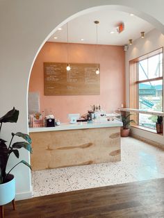 the interior of a coffee shop with pink walls and wooden counter top, potted plant in foreground