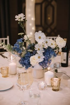 the table is set with white and blue flowers in vases, candles, and wine glasses