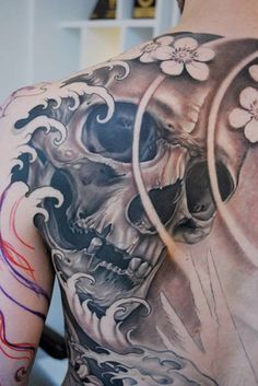 the back of a man's body with a skull and flowers tattoo on it