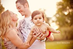 a woman holding a baby in her arms while standing next to two men and a girl