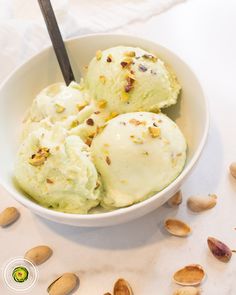 three scoops of ice cream in a white bowl with almonds around it on a table