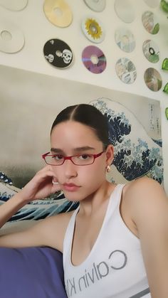 a young woman wearing glasses sitting on a bed with buttons all over the wall behind her