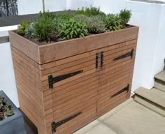 a wooden planter with plants growing out of it's sides on the side of a building