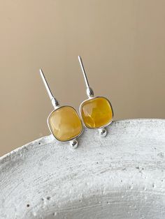 These handcrafted earrings, made from 925 silver and featuring an insert of natural Baltic amber, are elegantly adorned. A small ball-shaped element at the bottom and an oval bead at the top enhance the design, while the earrings are fastened with a hook closure for ease of wear. The geometric shapes and the blend of amber shades seamlessly become the perfect accent for any attire. The jewelry is presented in a unique piece. Sterling silver, amber 1,4" long Amber Earrings, Natural Amber, Amber Jewelry, Handcrafted Earrings, Conversation Starters, Earrings Collection, Baltic Amber, Hook Earrings, Sterling Earrings