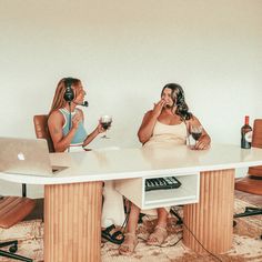 two women sitting at a table with laptops and headphones on, one talking on the phone