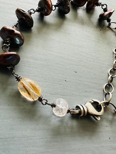 Handcrafted in Nashville, a wire wrapped chunky brown pearl bracelet.  Faceted gemstones and chunky brown keshi pearls were wrapped with blackened sterling silver wire to form a beautiful chain.  I chose a faceted mossy amethyst and a rutilated golden quartz gemstone. The pearls are a lovely brown with burgundy, purple, and blue nacre. So pretty.  Adjusts from 6-8.75 inches long.  Will fit smaller, more like 8.25 inches at the longest, due to the pearl and gem size.  Sterling silver rotating lob Rustic Hand Forged Brown Jewelry, Rustic Brown Hand Forged Jewelry, Pearl Charm Bracelet, Golden Quartz, Tudor Rose, Handmade Jewelry Designs, Keshi Pearls, Pearl Charms, Faceted Gemstones