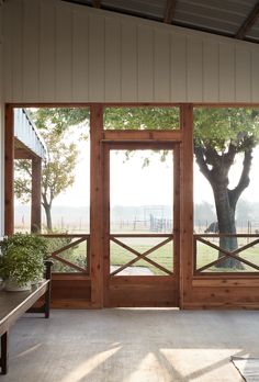 the inside of a house with large windows and wooden doors that lead out to an open field