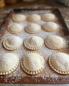 a baking tray filled with pastries covered in powdered sugar on top of a wooden table