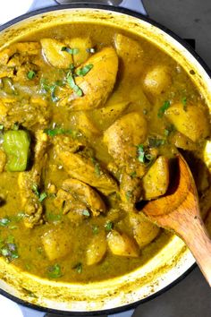 a pot filled with chicken and potatoes on top of a stove next to a wooden spoon