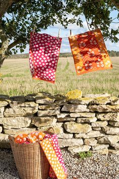 three colorful towels hanging from a clothes line in front of a stone wall and tree