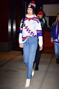 a woman walking down the street in jeans and an ice hockey jersey with letters on it