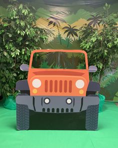 an orange jeep is on display in front of some trees and bushes with palm trees behind it