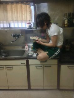 a person sitting on the kitchen counter reading a book