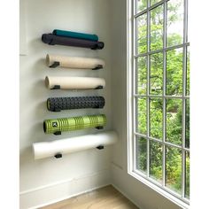 a wall mounted yoga mat rack in front of a window with several different types of yoga mats on it