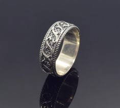 a silver ring with an intricate design on the outside and inside, sitting on a black surface