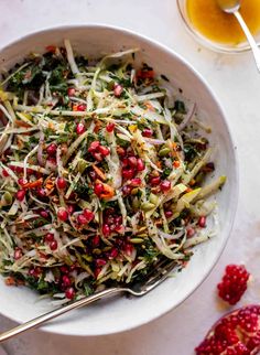 a white bowl filled with salad and topped with pomegranates next to a glass of orange juice