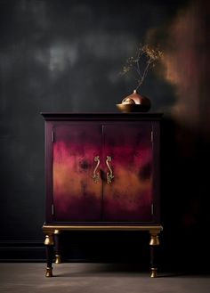 a red cabinet with two gold handles in front of a black wall and a vase on top