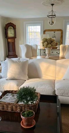 a living room filled with furniture and a clock on top of a table in front of two windows