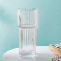 a clear glass sitting on top of a table next to a book and beaded necklace