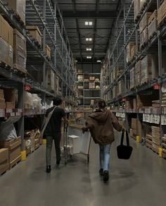 two people walking through a large warehouse with boxes on the shelves and luggage in hand