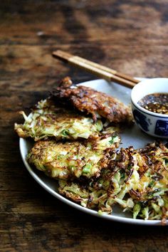 some food is on a plate with chopsticks and a bowl of dipping sauce